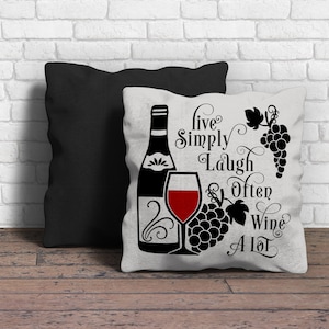May include: White pillow with black text that reads "Live Simply Laugh Often Wine A Lot". The pillow features a black silhouette of a wine bottle, a glass of red wine, and grapes.