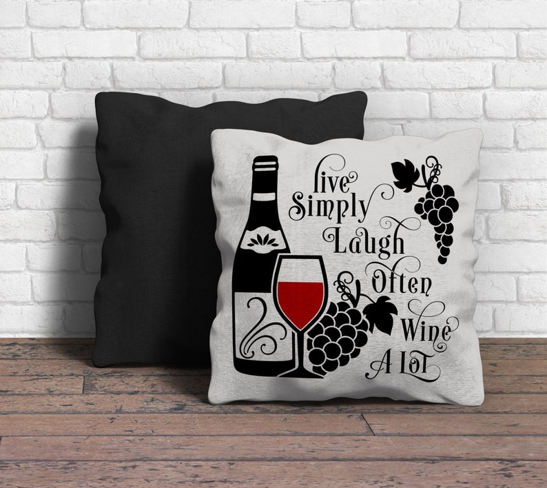 May include: White pillow with black text that reads "Live Simply Laugh Often Wine A Lot". The pillow features a black silhouette of a wine bottle, a glass of red wine, and grapes.