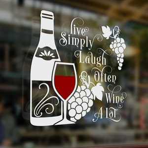 May include: White vinyl decal with a wine bottle, glass of wine, and grapes. The text reads "Live Simply Laugh Often Wine A Lot".