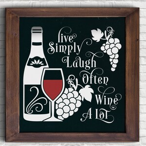 May include: A framed chalkboard sign with a white background and black text. The text reads "Live Simply Laugh Often Wine A Lot". The sign also features a white silhouette of a wine bottle, a wine glass, and grapes.