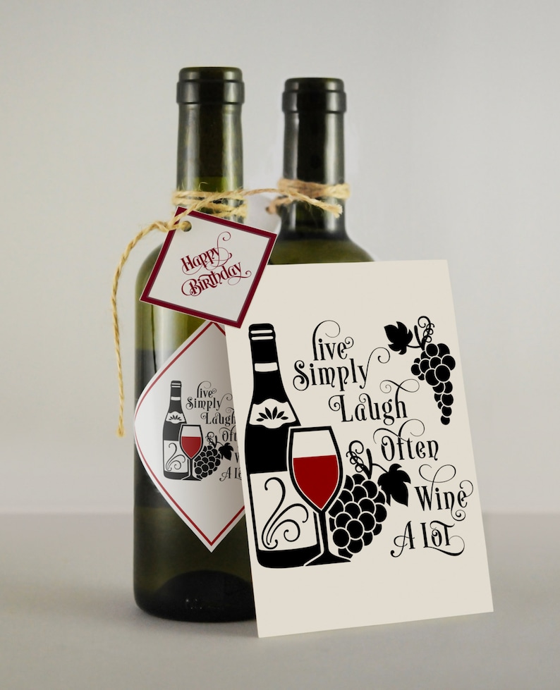 May include: Two bottles of wine with a gift tag that says "Happy Birthday". The gift tag is tied to the bottle with twine. A card with the text "Live Simply Laugh Often Wine A Lot" is in front of the bottles. The card has a black and white illustration of a wine bottle, a wine glass, and grapes.