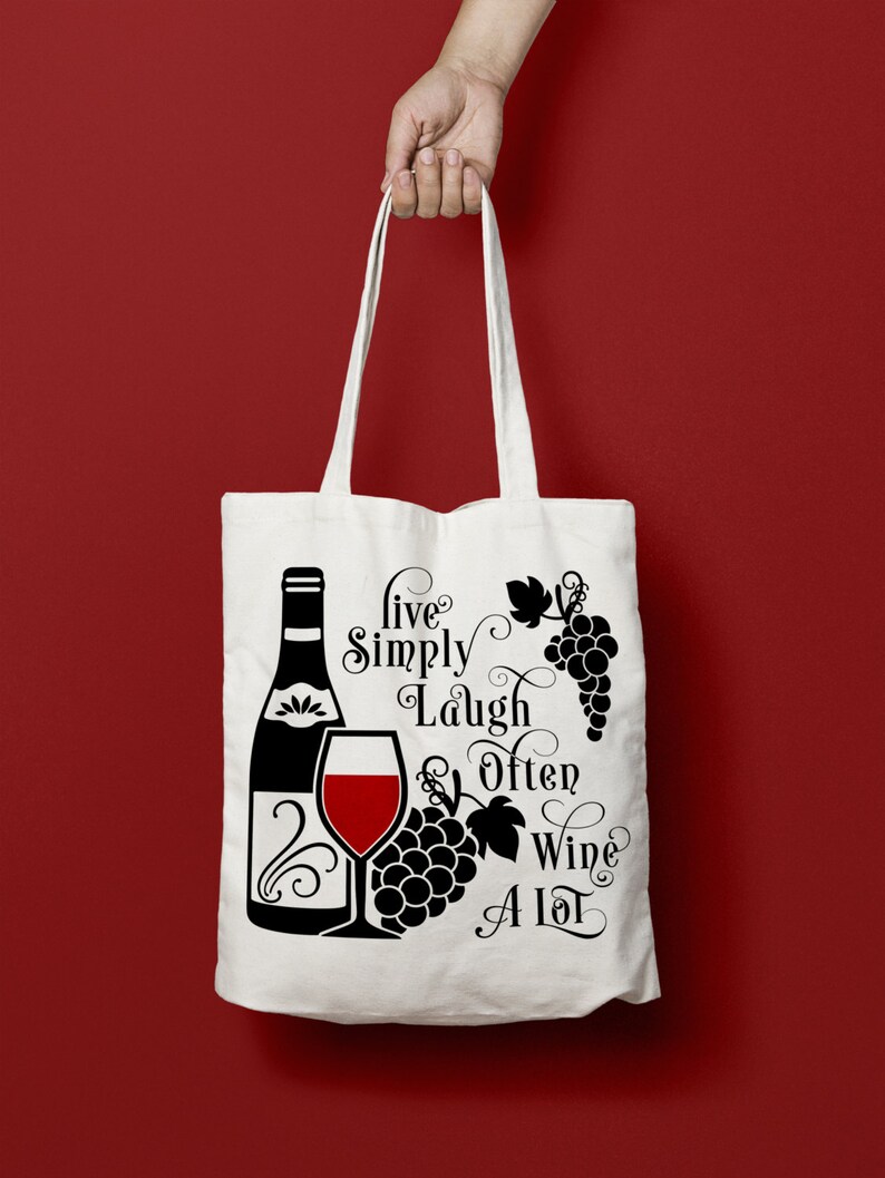 May include: White tote bag with black text and a graphic of a wine bottle, a glass of wine, and grapes. The text reads "Live Simply Laugh Often Wine A Lot".