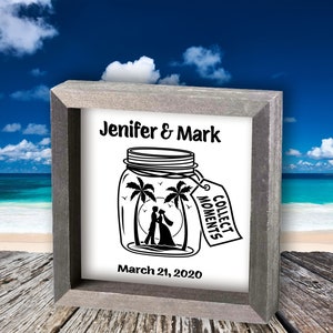 Può includere: Un cartello bianco incorniciato con un'illustrazione in bianco e nero di un barattolo di vetro con una coppia al suo interno. Il barattolo ha un'etichetta che dice "Collect Moments". Il cartello dice anche "Jenifer & Mark" e "March 21, 2020".