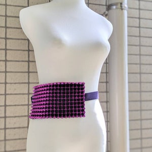 May include: A purple and black studded belt on a white mannequin. The belt is made of a grid of small, pointed studs.