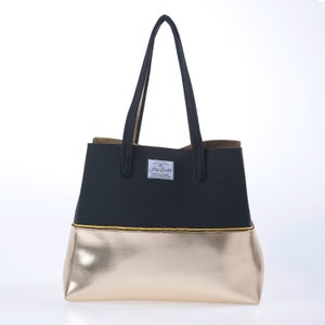 May include: A black and gold tote bag with a gold bottom and a black top. The bag has a yellow trim and a white label with the text "Sea Love" on it.