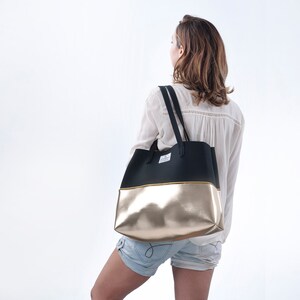 May include: A black and gold tote bag with a black strap. The bag has a gold bottom and a black top.