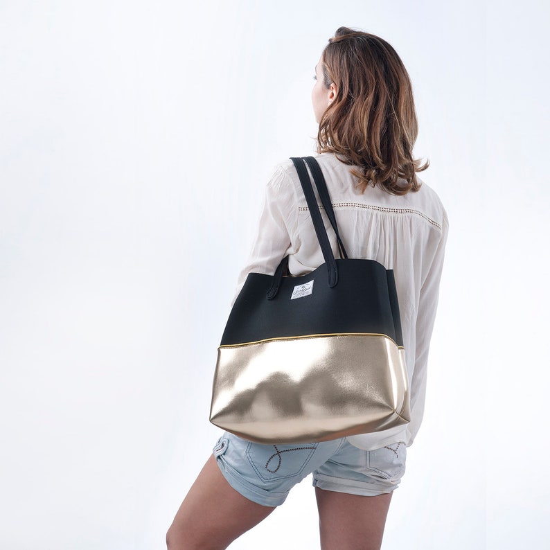 May include: A black and gold tote bag with a black strap. The bag has a gold bottom and a black top.