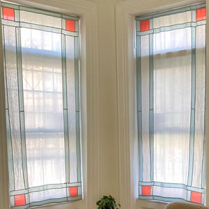 May include: A cozy corner with two windows featuring stained glass-style panels in red, blue, and white. A small round table holds plants, and a cream-colored, fluffy armchair with a decorative pillow sits nearby. The room has hardwood floors.