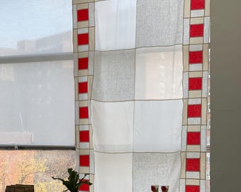 May include: A window curtain with a geometric design of white, gray, and red squares. A table is set with various items, including cups, jars, wooden spoons, and a small plant, all arranged on a blue tablecloth.
