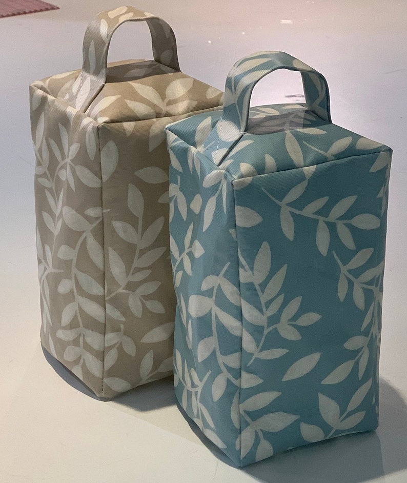 Puede incluir: Dos tapones de puerta con asas. Uno es beige con un patr&oacute;n de hojas blancas y el otro es azul con un patr&oacute;n de hojas blancas.