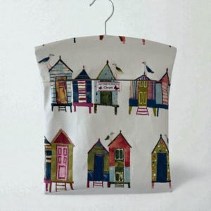 Bolsa para pregadores de roupa em lona encerada com estampa de cabanas de praia – Design litorâneo.