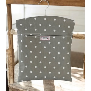 Puede incluir: Una funda de ropa gris con lunares blancos, colgada de una percha metálica. La funda tiene un bolsillo con cremallera y una etiqueta que dice "ALL THINGS PRETTY Designs". La funda se muestra en una silla de madera.