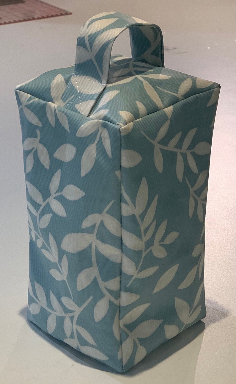 Puede incluir: Un tope de puerta azul claro con un patr&oacute;n de hojas blancas y un asa de tela.