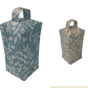 Puede incluir: Dos topes de puerta con un patr&oacute;n de hojas. Uno es azul claro con hojas blancas y el otro es beige con hojas blancas. Ambos tienen un asa de tela.