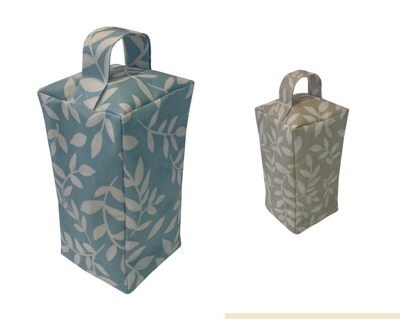 Puede incluir: Dos topes de puerta con un patr&oacute;n de hojas. Uno es azul claro con hojas blancas y el otro es beige con hojas blancas. Ambos tienen un asa de tela.