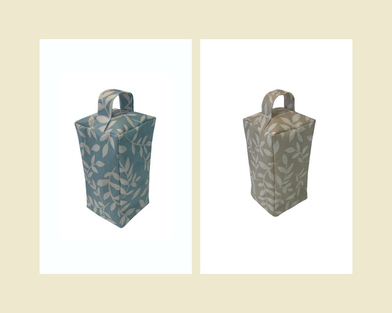 Puede incluir: Dos topes de puerta con un patr&oacute;n de hojas. Uno es azul con hojas blancas y el otro es beige con hojas blancas.