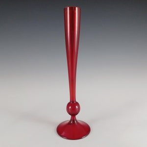 May include: A tall, red glass vase with a round base and a slender neck.