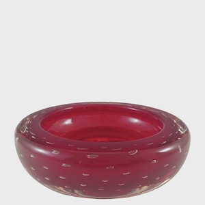 Può includere: Una ciotola rotonda in vetro rosso rubino con base trasparente. La ciotola ha una finitura liscia e lucida ed è punteggiata da piccole bolle trasparenti. Il design della ciotola è semplice ed elegante, adatta per uso decorativo.