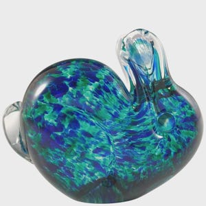 May include: A decorative glass sculpture in the shape of a snail. The snail's body is a mix of blue and green colors, with a clear, curved horn and a clear, rounded tail. The glass has a glossy finish.
