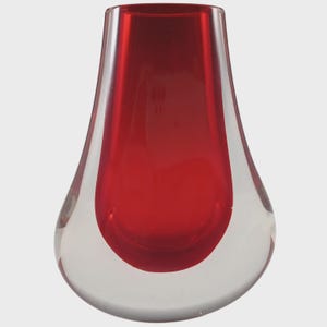 May include: A clear glass vase with a teardrop shape. The interior is a vibrant red, contrasting with the transparent exterior. The vase has a smooth, polished finish, suitable for home decor.