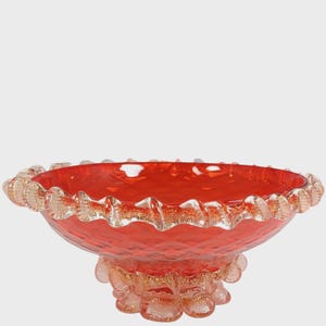 Op de afbeelding: Een helderrode glazen kom met een gerimpelde rand en een decoratieve voet. De kom heeft een textuur en een transparante, goudkleurige rand. Deze decoratieve kom is ideaal om te serveren of tentoon te stellen.