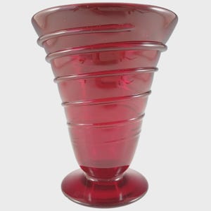 May include: A translucent ruby red glass vase featuring a wide, flared rim and a tapered body. The exterior surface is decorated with a continuous, raised glass coil that spirals around the entire circumference from the base to the top rim.