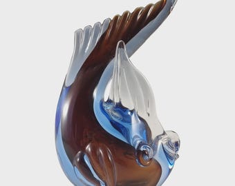 May include: A glass sculpture of a seal in shades of brown, blue, and clear. The seal is arched, with its tail and flippers extended. The sculpture has a smooth, glossy finish and is set against a white background.