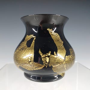 May include: A black glass vase with gold leaf accents. The vase has a rounded body and a flared opening.