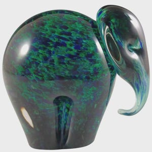 May include: A glass elephant sculpture in shades of green and blue. The elephant has a rounded body and a curved trunk. The glass has a speckled pattern, giving it a unique texture. The sculpture is a decorative item.