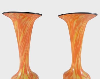 May include: Two orange glass vases with yellow streaks and a black rim. The vases have a flared top and a rounded base. The design is reminiscent of a sunset. These decorative vases are perfect for displaying flowers or as a standalone art piece.
