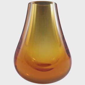 May include: A teardrop-shaped glass vase featuring a smooth, translucent gradient that transitions from a deep amber hue at the rounded base to a lighter, golden yellow tone near the open, circular top, showcasing a polished, reflective surface.