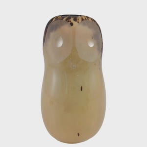 May include: A decorative owl figurine with a light brown body and a speckled, dark brown top. The owl has two large, round eye openings. The figurine is made of a translucent material.