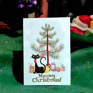 Carte de chat de Noël d'arbre de Noël de chat noir. Chat noir assis sous l'arbre vérifiant les cadeaux "Meowy Christmas"©