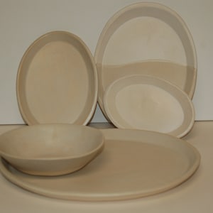 May include: Set of four beige ceramic dishes, including a large oval platter, a smaller oval dish, a round bowl, and a smaller oval dish.