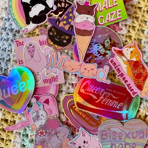 May include: A collection of colourful stickers featuring various designs, including cats, a witch, an ice cream cone, a can of soda, and text phrases like "Queer Femme", "Bisexual babe", and "Don't forget to refill ur meds, baby."