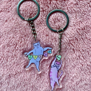 May include: Two cat-shaped keyrings with silver key rings. The blue cat keyring has the words "dream" and "team" on hearts. The purple cat keyring has the word "team" on a heart.