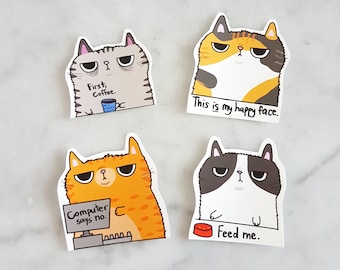 May include: Four cat stickers with different expressions and text. The first sticker shows a grey cat with the text "First, Coffee." The second sticker shows a calico cat with the text "This is my happy face." The third sticker shows an orange cat with the text "Computer says no." The fourth sticker shows a black and white cat with the text "Feed me."