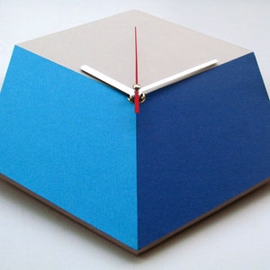 Pu&ograve; includere: Un orologio geometrico con un quadrante bianco, blu e blu chiaro. Le lancette dell'orologio sono argentate e rosse.