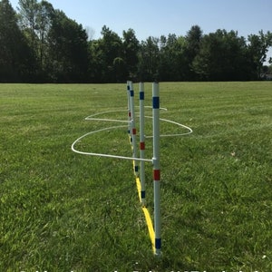 May include: A set of four white poles with blue and red tape markings, used for agility training. The poles are set up in a line on a grassy field with a yellow tape line running along the ground. Guide wires only. Poles NOT included.