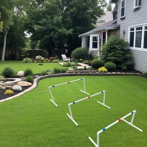 May include: Three white adjustable dog agility hurdles with red and blue accents. The hurdles are set up on a green grassy lawn.