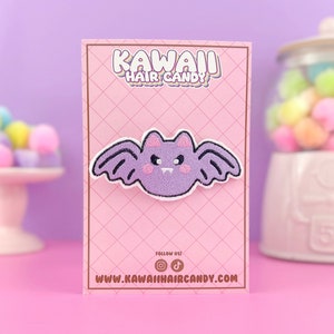 May include: Purple and black embroidered bat patch with a pink face and white eyes. The patch is on a pink card with the text "Kawaii Hair Candy" and a website address.