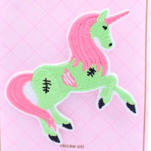 Puede incluir: Parche de hierro bordado verde y rosa de un unicornio zombie con puntadas y una melena rosa. "Follow Us!" est&aacute; escrito en la parte inferior del parche.