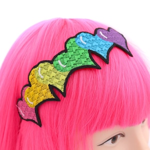May include: A rainbow-colored heart headband with a textured fabric. The headband is made of five hearts, each a different color of the rainbow.