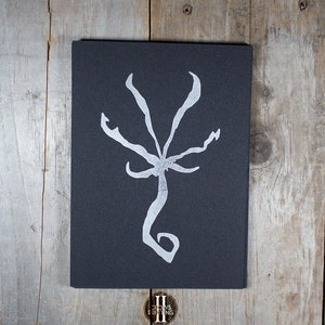May include: A black card with a white, stylized, five-pointed star design. The card is on a wooden surface.