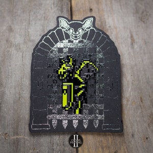 May include: A black and yellow enamel pin featuring a pixelated character in front of a black and white castle gate with a bat above the gate. The pin has the text "Crows Printing" at the bottom.