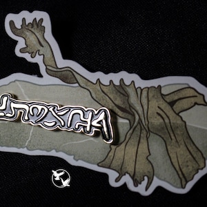 May include: Gold-colored enamel pin with the word "MYTH" written in a stylized font. The pin is on a white background with a drawing of a tree branch.