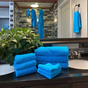 May include: A bathroom vanity with a mirror, a sink, and a set of blue towels. The towels are folded and stacked on the counter.