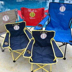 Pu&ograve; includere: Cinque sedie pieghevoli personalizzate a tema baseball. Le sedie sono blu, rosse, beige e blu scuro con bordi gialli. Ogni sedia ha una palla da baseball e un nome ricamato sullo schienale.