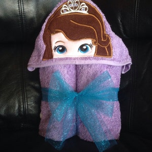 May include: Purple hooded towel with a princess character embroidered on the hood. The towel is tied with a blue sparkly ribbon.