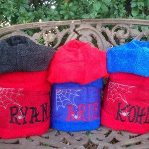 Puede incluir: Tres toallas con capucha con telara&ntilde;as bordadas y nombres: Ryan, Brie y Kohl. Las toallas son rojas, azules y negras.